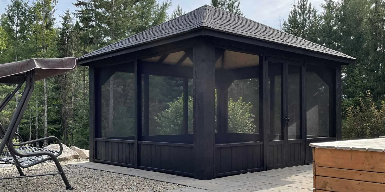 Gazébo noir dont les panneaux moustiquaires viennent d’être remplacés, terrasse avec spa en arrière-plan