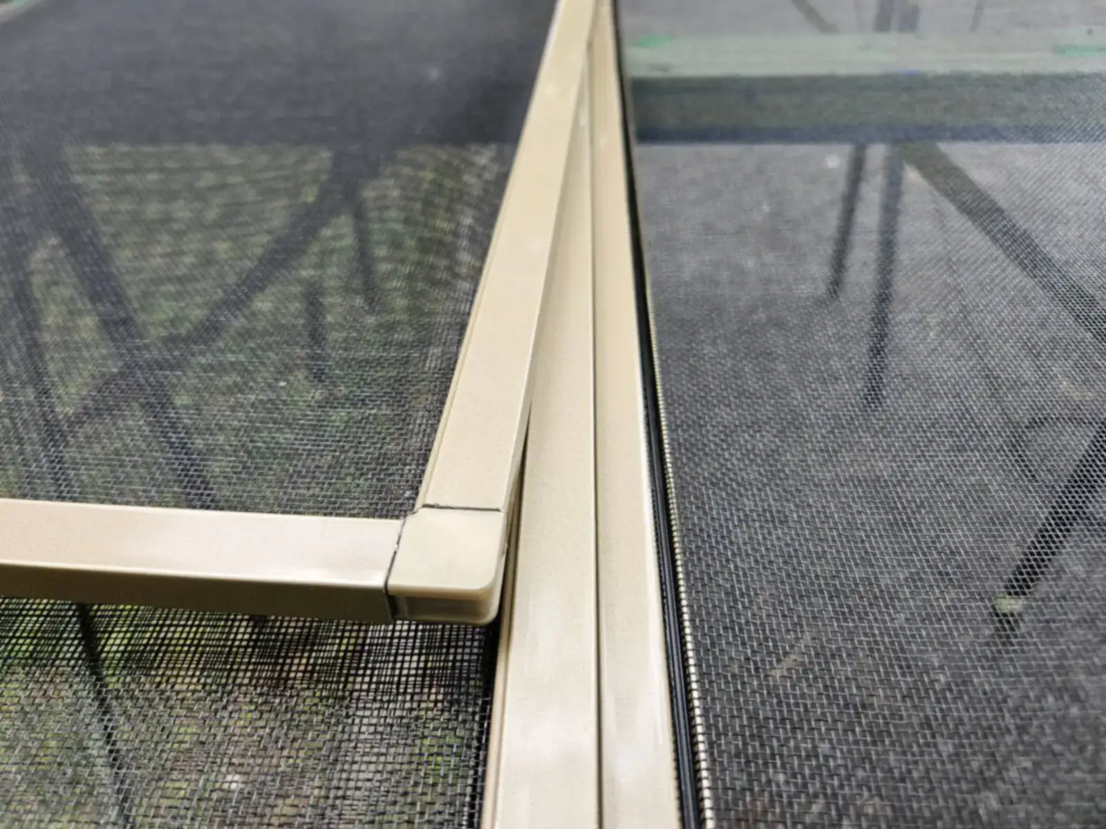 Deux moustiquaires à cadre d’aluminium beige dans la glissière d’une fenêtre, toile de fibre de verre noire